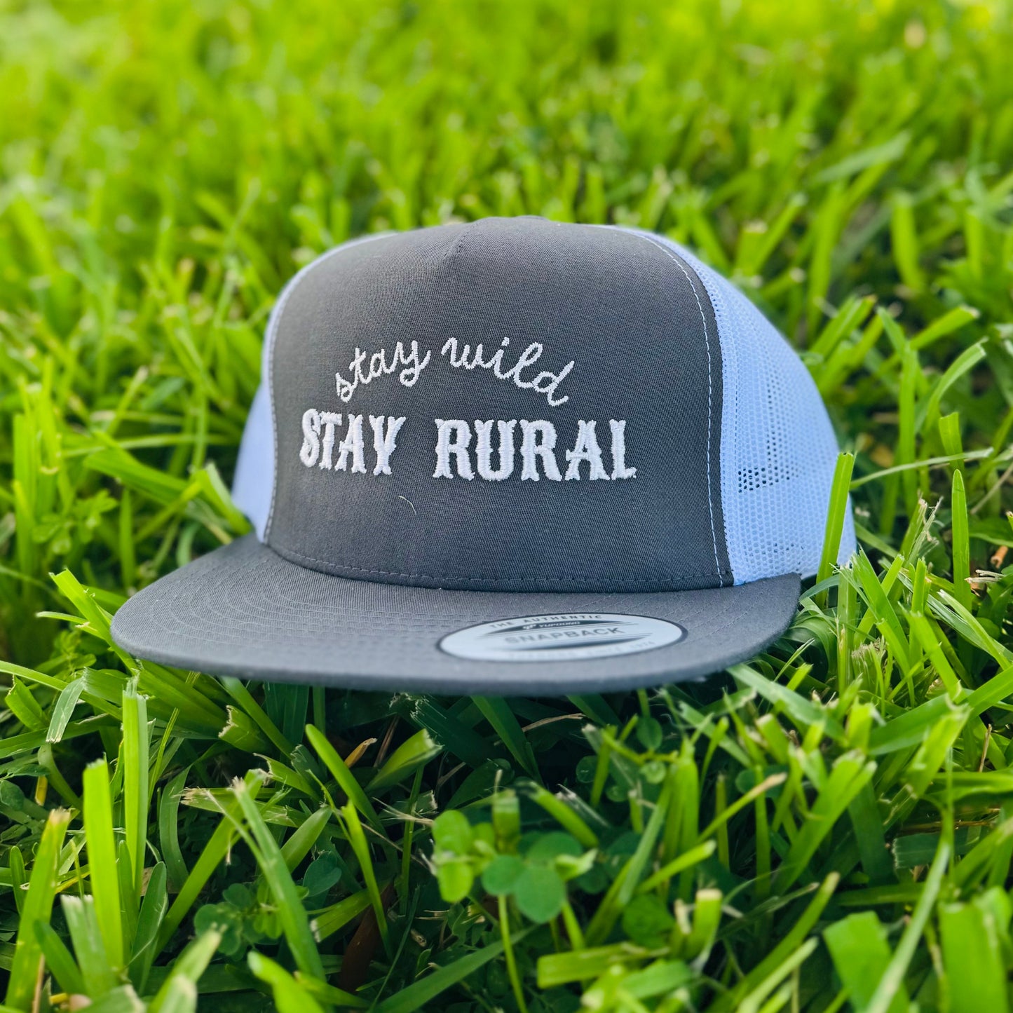Gray and blue cap with 'stay wild stay rural' text on grass
